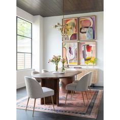 a dining room table with four chairs and paintings on the wall behind it, along with an area rug