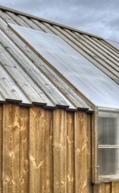 a wooden building with a metal roof and window on the side, in front of a cloudy sky