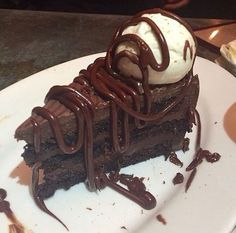 a piece of chocolate cake with ice cream on top and drizzled in chocolate