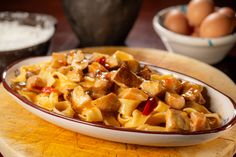 a bowl filled with pasta and meat on top of a wooden table next to eggs