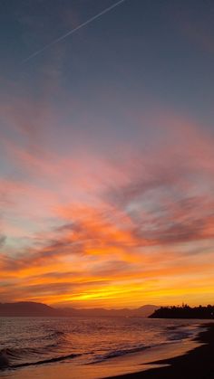 the sun is setting over the ocean with clouds in the sky and on the beach