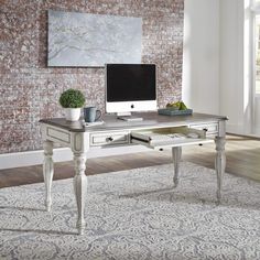 a desk with a computer on top of it in front of a brick wall and rug