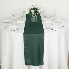 the table is set with white plates and wine glasses on it, along with a green runner