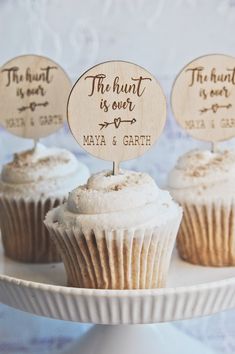 three cupcakes with wooden signs on them sitting on a cake platter that says the hunt is over