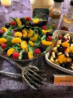 a table topped with plates filled with fruit and salad next to condiments on top of a cloth covered table