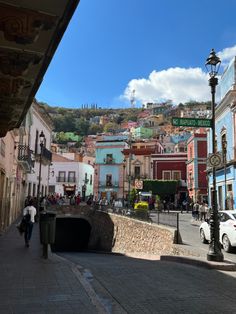 people walking down the street in front of colorful buildings on a hill behind them is a lamp post