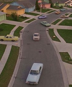 an aerial view of cars driving down the street in front of houses and buildings with green grass