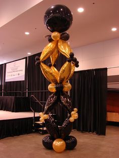 a balloon sculpture in the middle of a room with black drapes and gold balloons