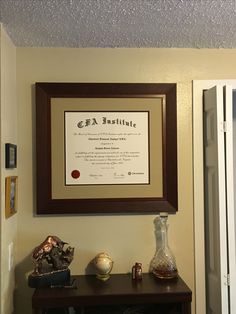 a framed certificate hangs on the wall above a table with vases and other items