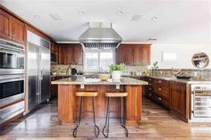 a large kitchen with wooden cabinets and stainless steel appliances, along with two bar stools