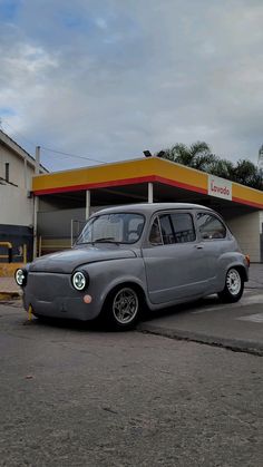 an old grey car parked in front of a gas station