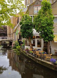 a river running through a small town next to tall buildings and tables with chairs on them