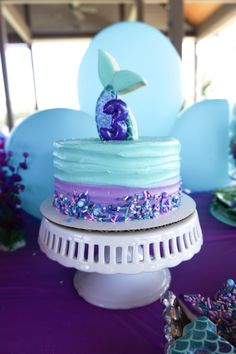 a blue and purple cake sitting on top of a white pedestal next to other decorations