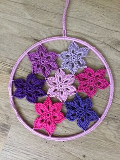 four crocheted flowers are hanging from a circular ornament on a wooden table