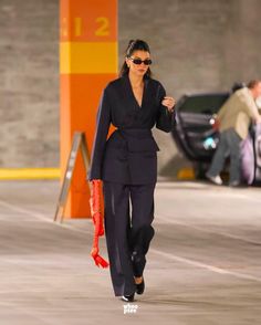 a woman walking down the street in a black suit and red heels with her hand on her hip