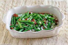 green beans with bacon and onions in a white dish on a tableclothed surface