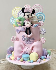 a birthday cake with a minnie mouse on top and candy decorations around the bottom tier