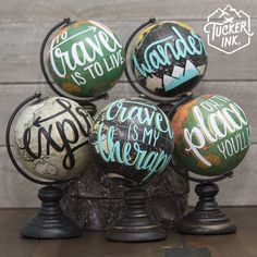 four globes with words painted on them sitting on top of a wooden table next to each other