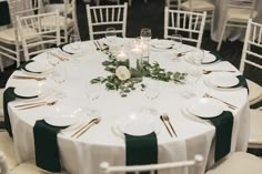 the table is set with white and green linens, silverware, candles and greenery