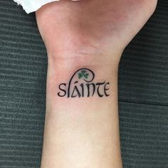 a person with a small tattoo on their wrist that says slante and shamrock leaves