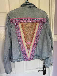 a denim jacket with an embroidered triangle on it hanging from a hook in front of a door