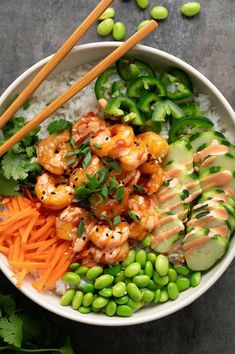 a bowl filled with rice, carrots and shrimp next to chopsticks on the side