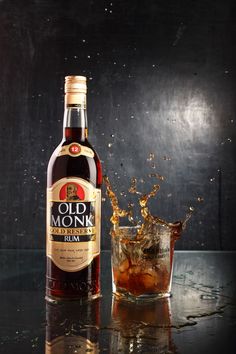 a bottle and glass filled with liquid on top of a black table next to a dark background