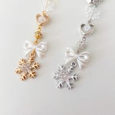 two snowflakes with hearts and bows are hanging from chains on a white surface