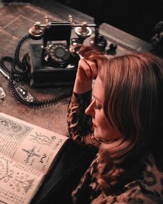 a woman sitting in front of an open book with writing on the pages next to a telephone