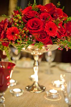 a vase filled with red flowers sitting on top of a table next to silver candles