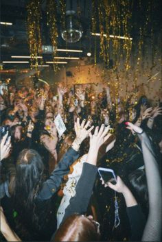 a group of people at a party with their hands in the air and confetti falling from the ceiling