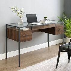 a laptop computer sitting on top of a wooden desk next to a plant in a vase