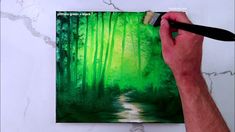 a man is painting a forest scene with green colors on the canvas, and holding a brush in his left hand