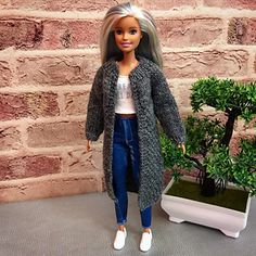 a doll is standing next to a potted plant and wearing a gray cardigan