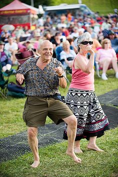 an older man and woman dancing in front of a crowd at a music festival on their cell phones