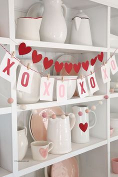 valentine's day decorations on shelves in a kitchen with white dishes and pink cups