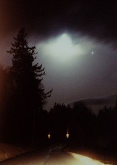 the night sky is dark and cloudy, with some lights shining on the road below