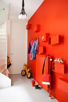 an orange wall in a white room with red shelves and toys on the floor next to it