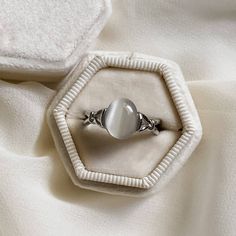 a ring with a white stone in it sitting on top of a cloth covered box