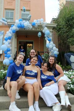 a group of young women sitting on steps in front of a building with blue and white balloons