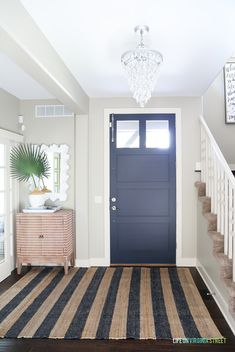 a blue front door is flanked by a striped rug and a chandelier in this entryway