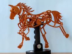 an orange metal horse sculpture sitting on top of a wooden table