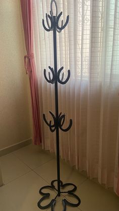 a black metal coat rack in front of a window with white curtains and pink drapes