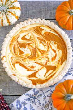 a pumpkin pie with swirly cream in the middle on a wooden table surrounded by fall decorations