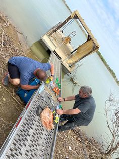 two men standing on the edge of a dock next to a body of water,