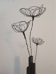 three metal flowers in a black vase on a white surface with wires attached to the stems