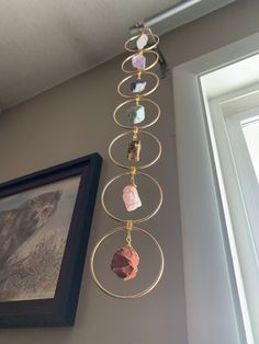 a wall hanging with different colored stones on it's side next to a window