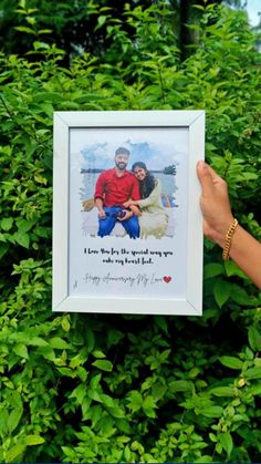 a person holding up a framed photo in front of some bushes