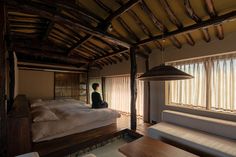 a person sitting on top of a bed in a room with wooden floors and walls