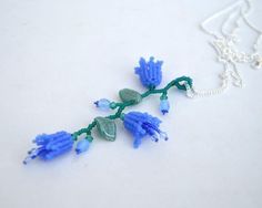 a necklace with blue flowers and beads on a white surface, hanging from a silver chain